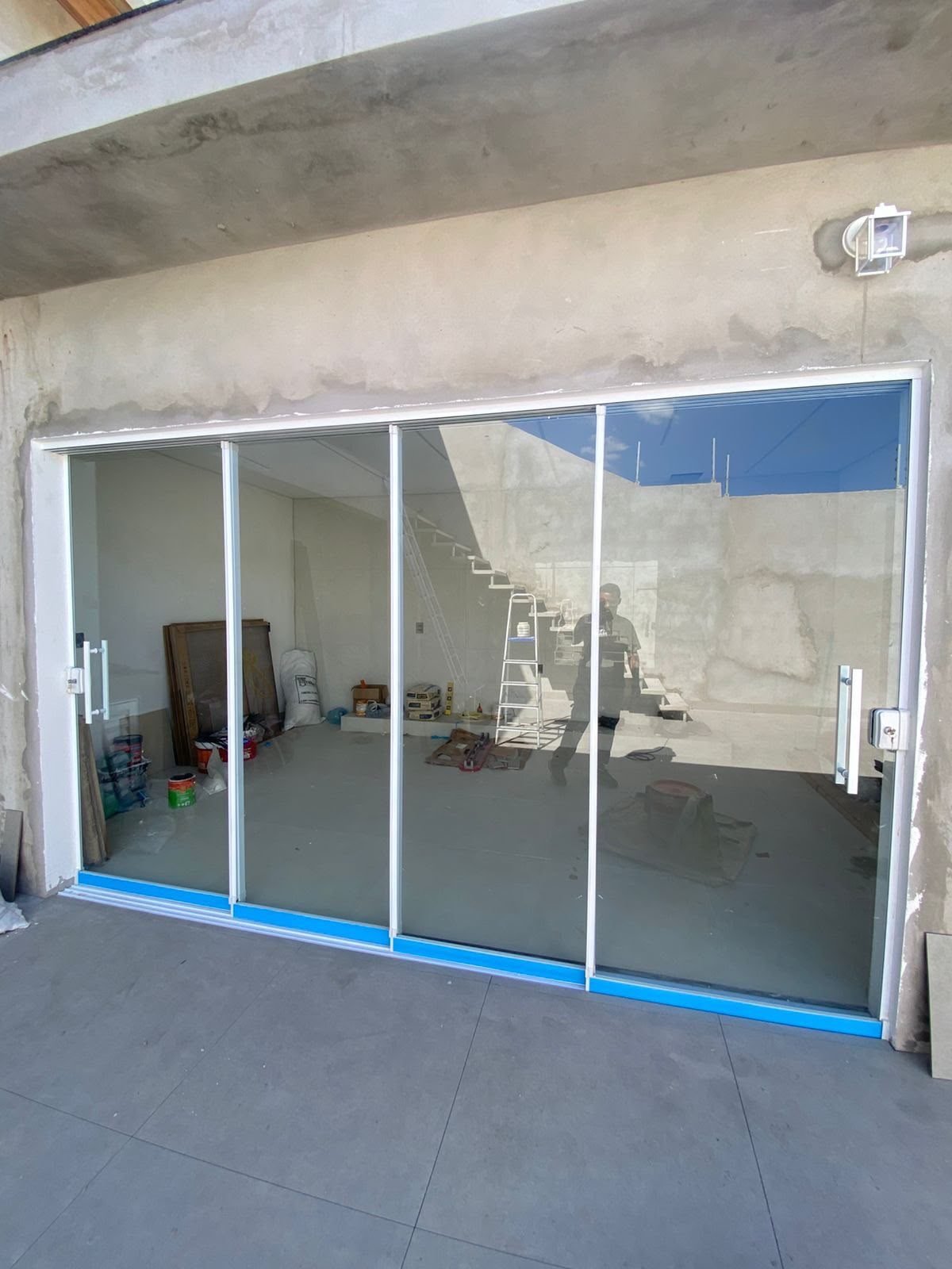 Porta de vidro de quatro folhas com perfil de alumínio branco, recém-instalada em uma obra